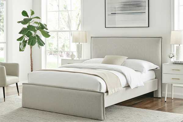 White bedframe in bedroom with cream bedding and cushions.